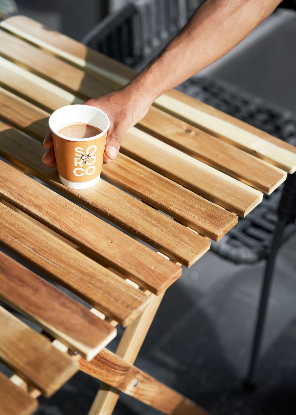A Soroco takeaway cup on a slatted wooden table